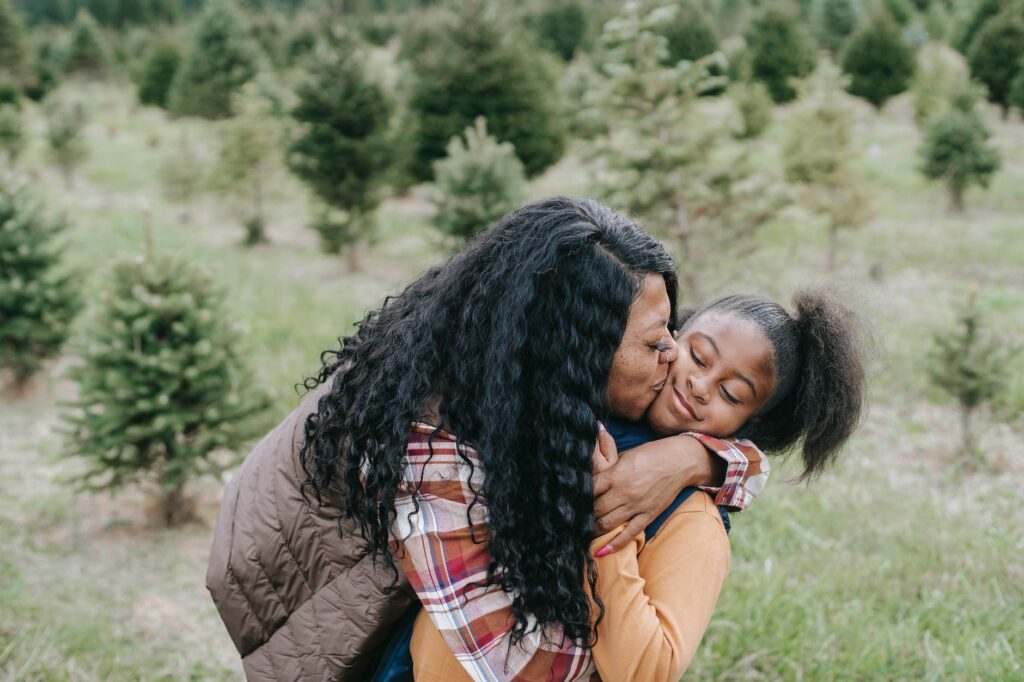 happy black mother embracing and kissing daughter