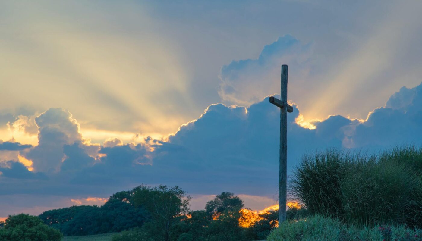 big wooden cross on green grass field under the white clouds
