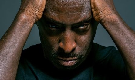 man in blue crew neck shirt holding his head with both hands