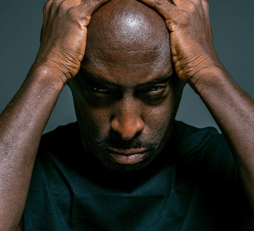 man in blue crew neck shirt holding his head with both hands